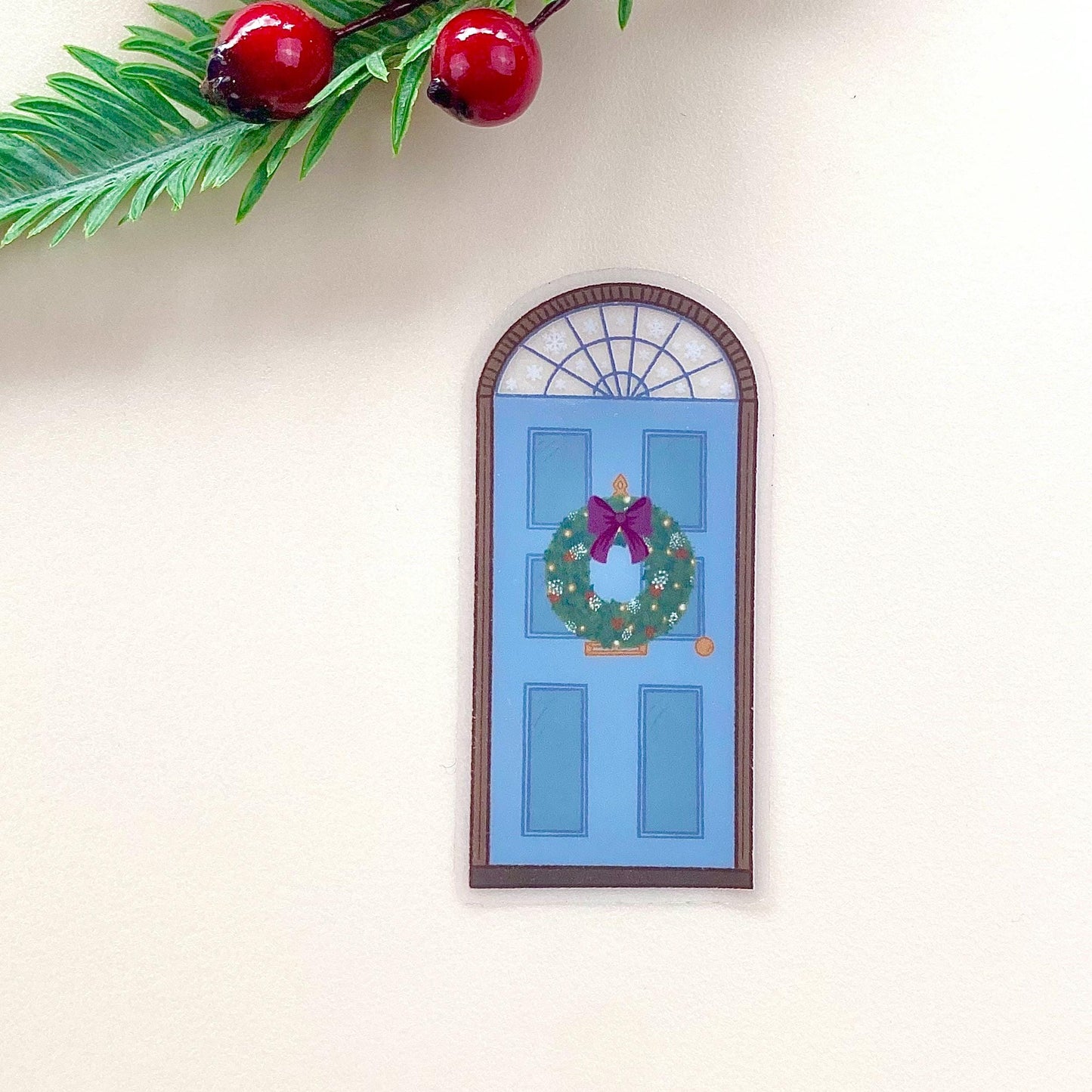 A sticker with a blue door decorated for Christmas against a cream background.