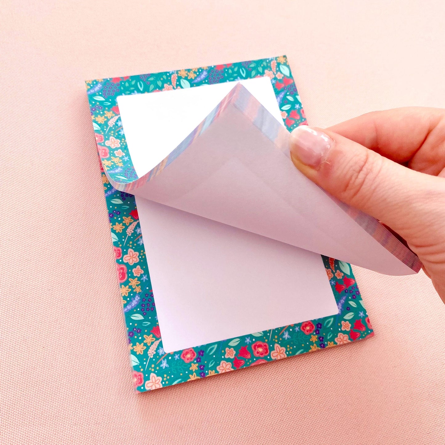 Hand peeling a sheet of paper off a floral-patterned note pad.