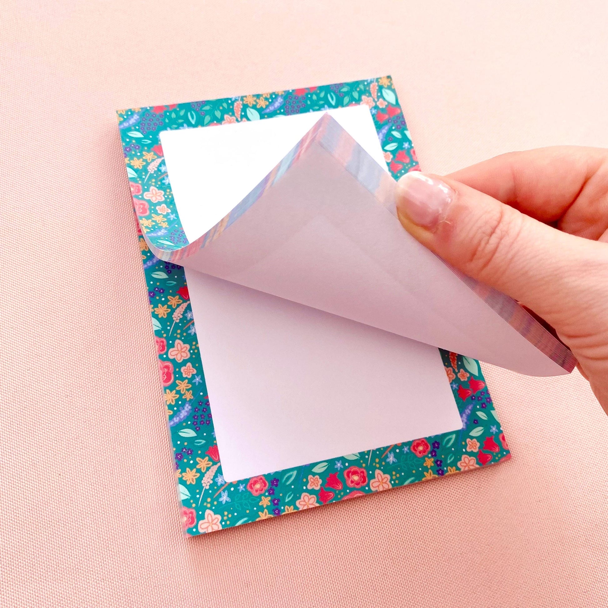 Hand peeling a sheet of paper off a floral-patterned note pad.