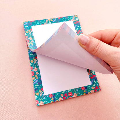 Hand peeling a sheet of paper off a floral-patterned note pad.
