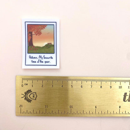 Small polaroid sticker with autumn scene and text next to a ruler for scale.