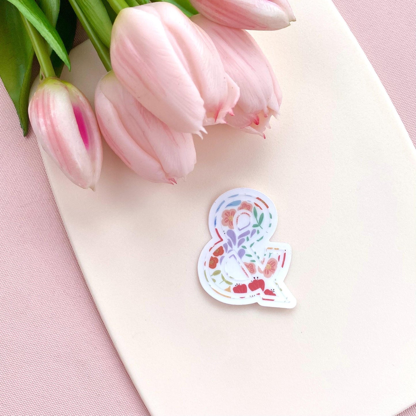 Floral sticker with an ampersand on a pink surface with tulips