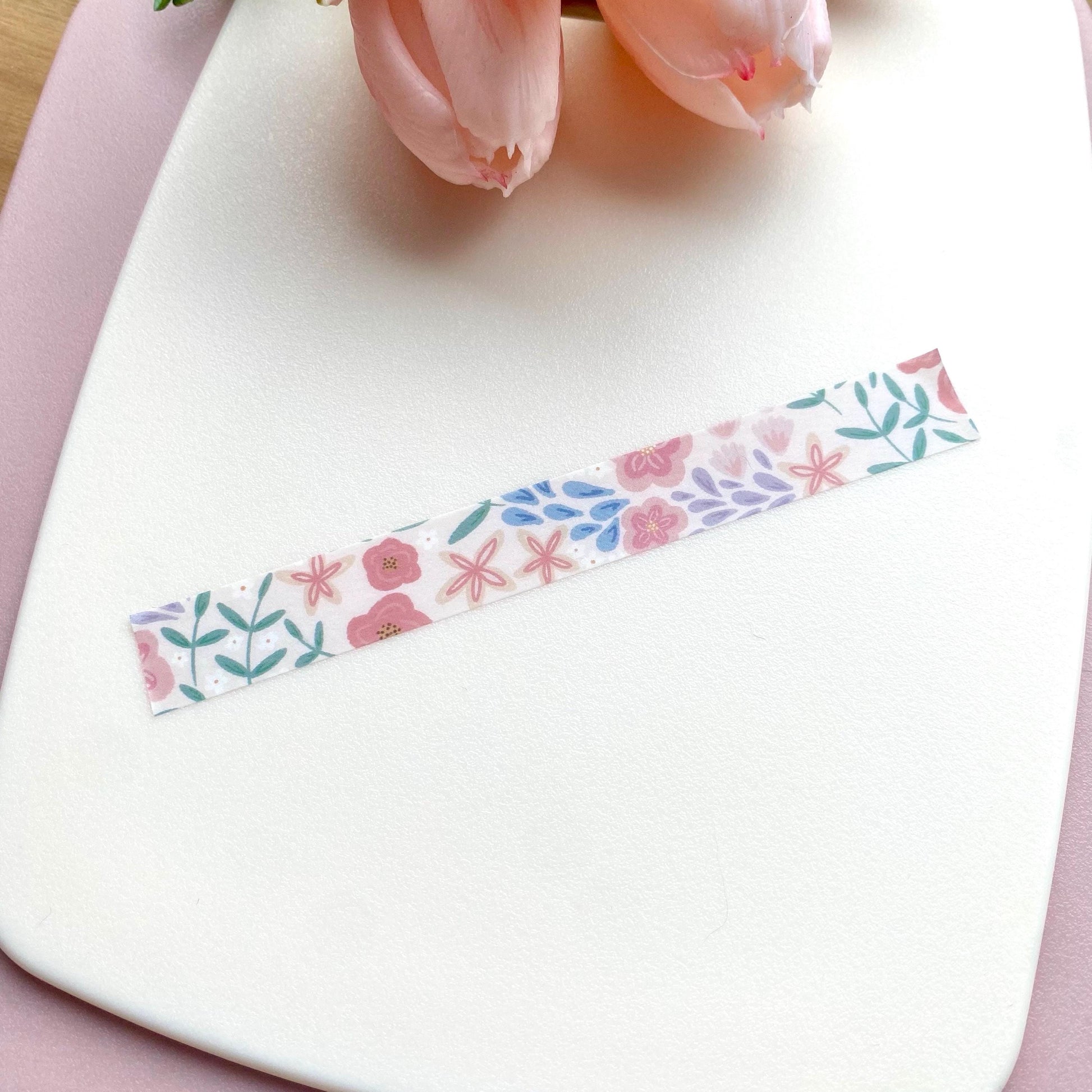 Floral washi tape on a white surface with pink flowers in the background
