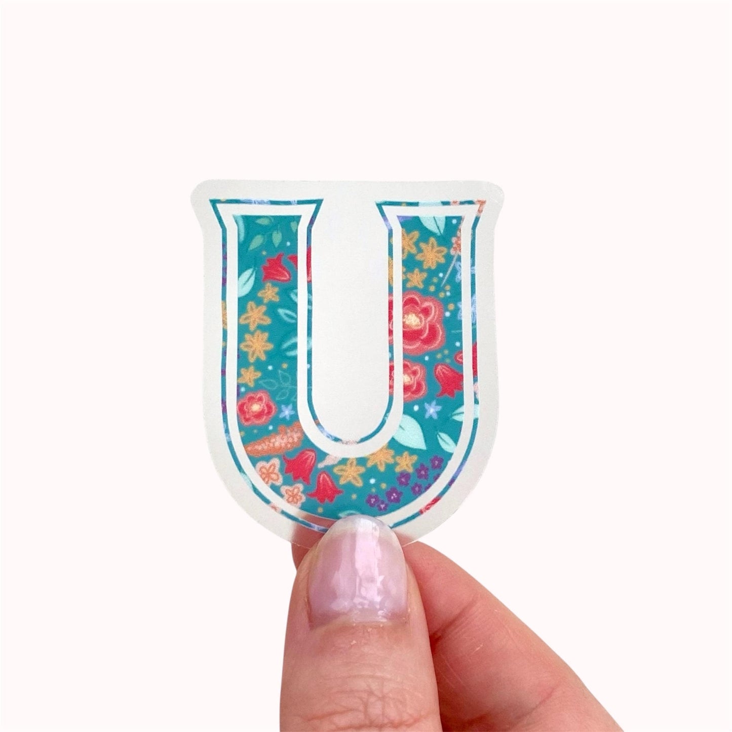 Colourful letter 'U' sticker with floral pattern held by a hand on a white background