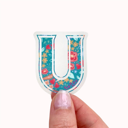 Colourful letter 'U' sticker with floral pattern held by a hand on a white background