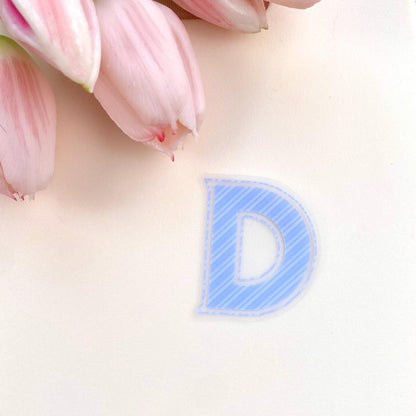 Blue striped  letter 'D' sticker on a light pink background with pink tulips