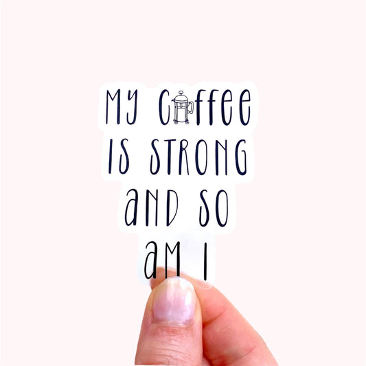 Hand holding a transparent sticker with 'My coffee is strong and so am I' text against a white background