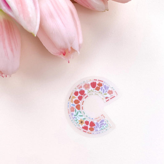Floral-patterned letter 'c' sticker on a light pink background with pink tulips.