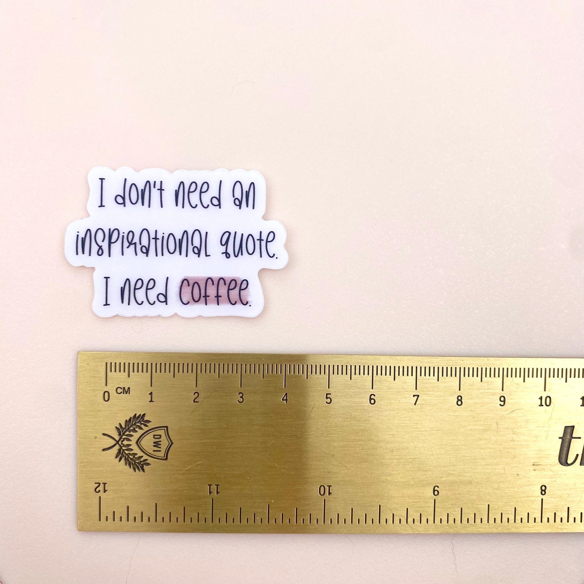 Sticker with 'I don't need an inspirational quote, I need coffee' text next to a ruler on a beige background