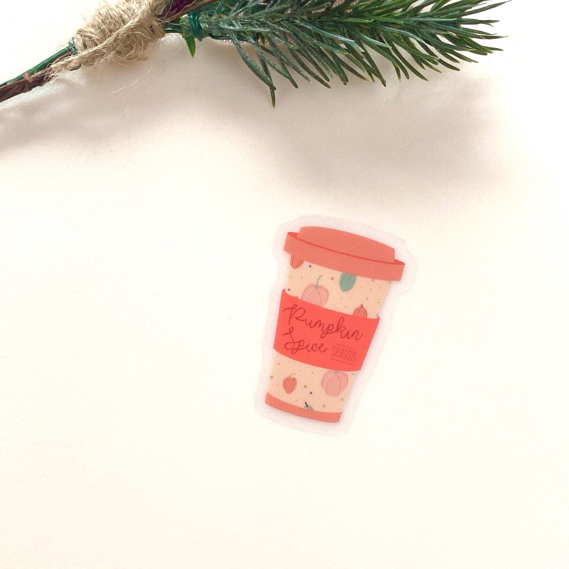 Decorative pumpkin spice coffee cup sticker on a white background with greenery.