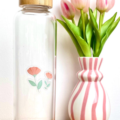 Pink flowers sticker against a glass bottle besides a pink striped vase of tulips.