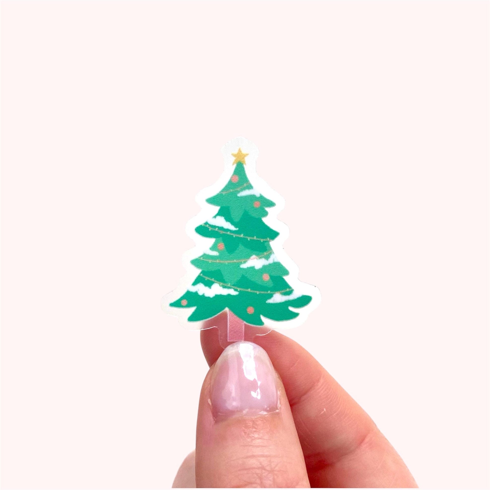 Hand holding a small green Christmas tree sticker with a star on a white background