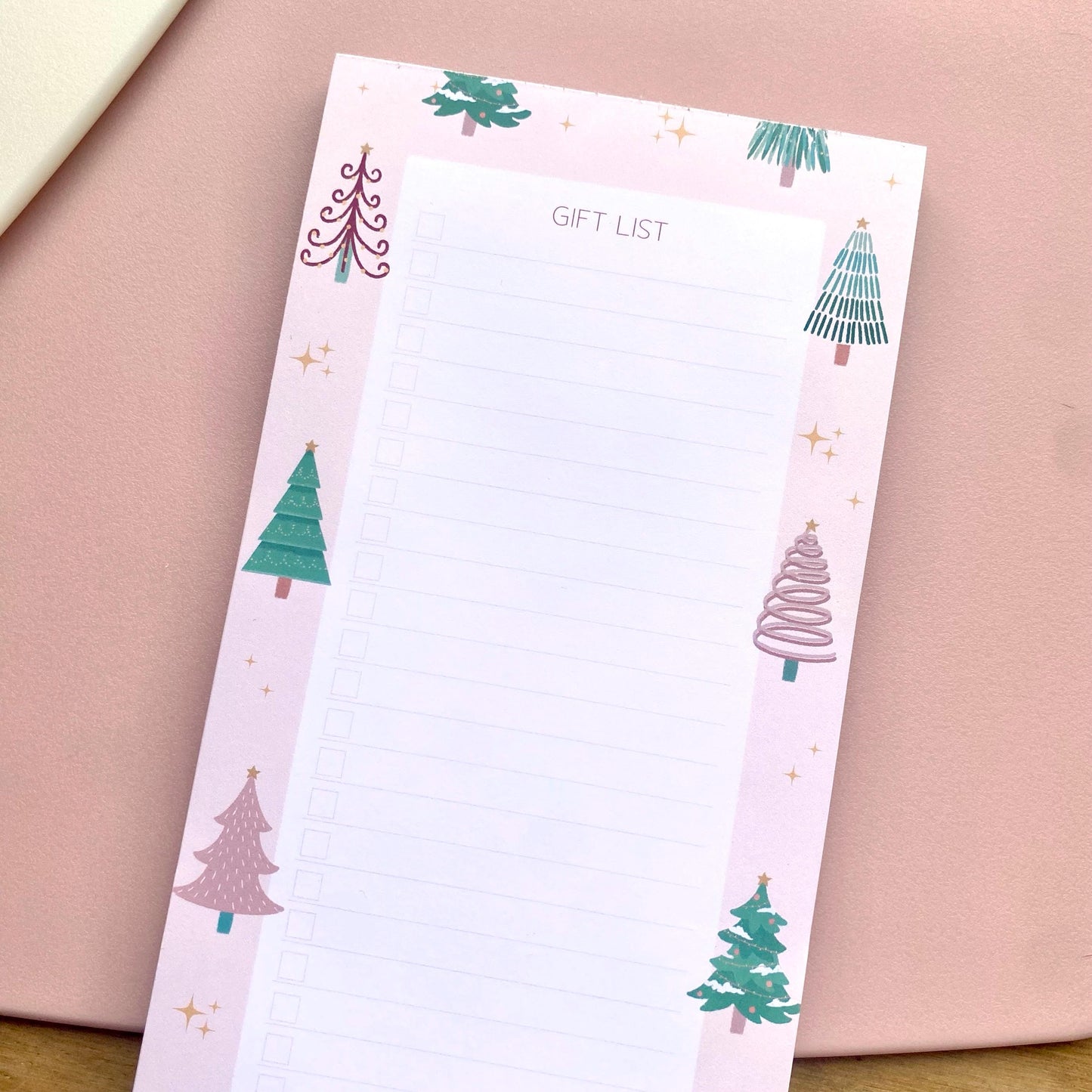 Notepad with Christmas tree designs on a pink surface