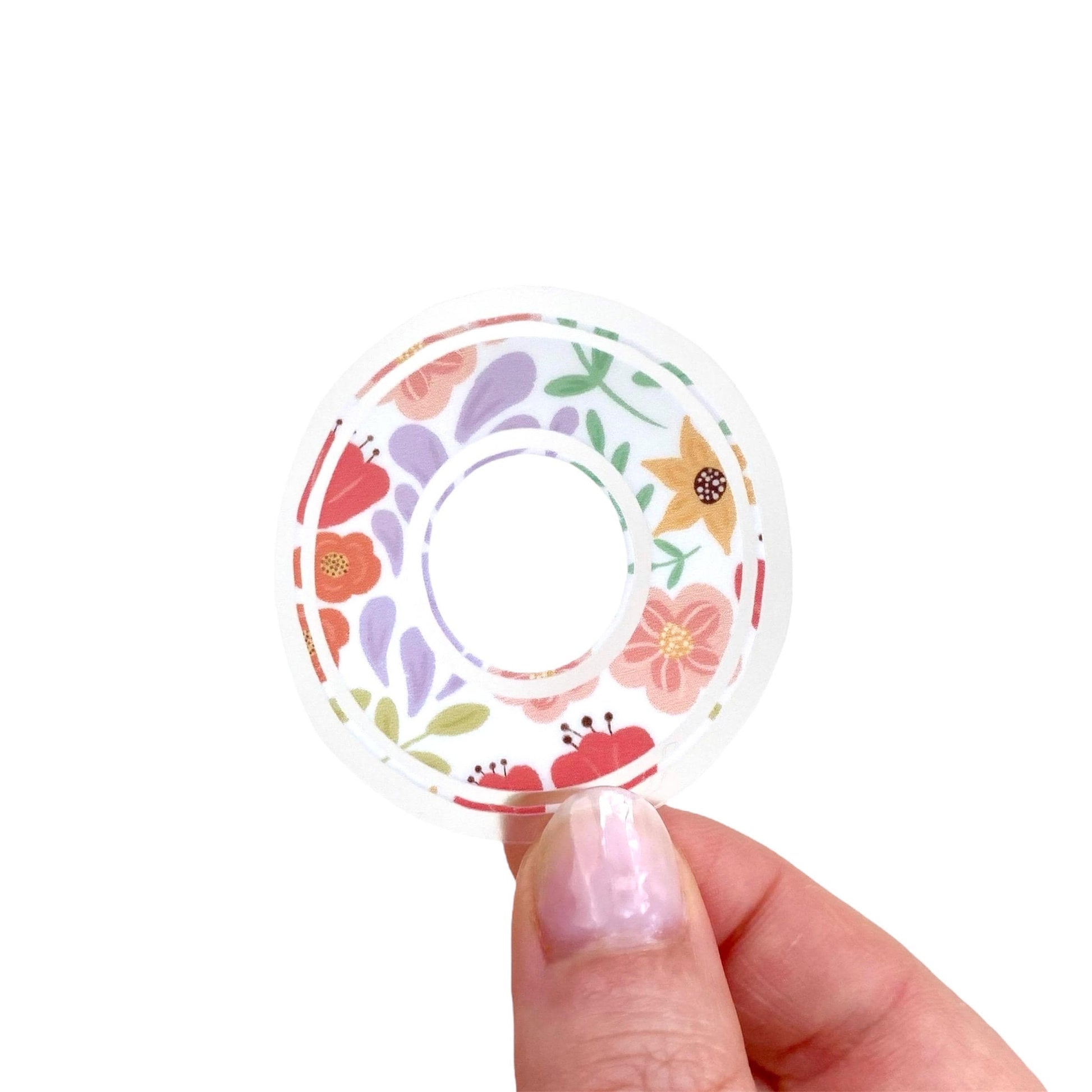 Decorative letter 'O' sticker with floral patterns held between fingers against a light background.
