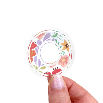 Decorative letter 'O' sticker with floral patterns held between fingers against a light background.
