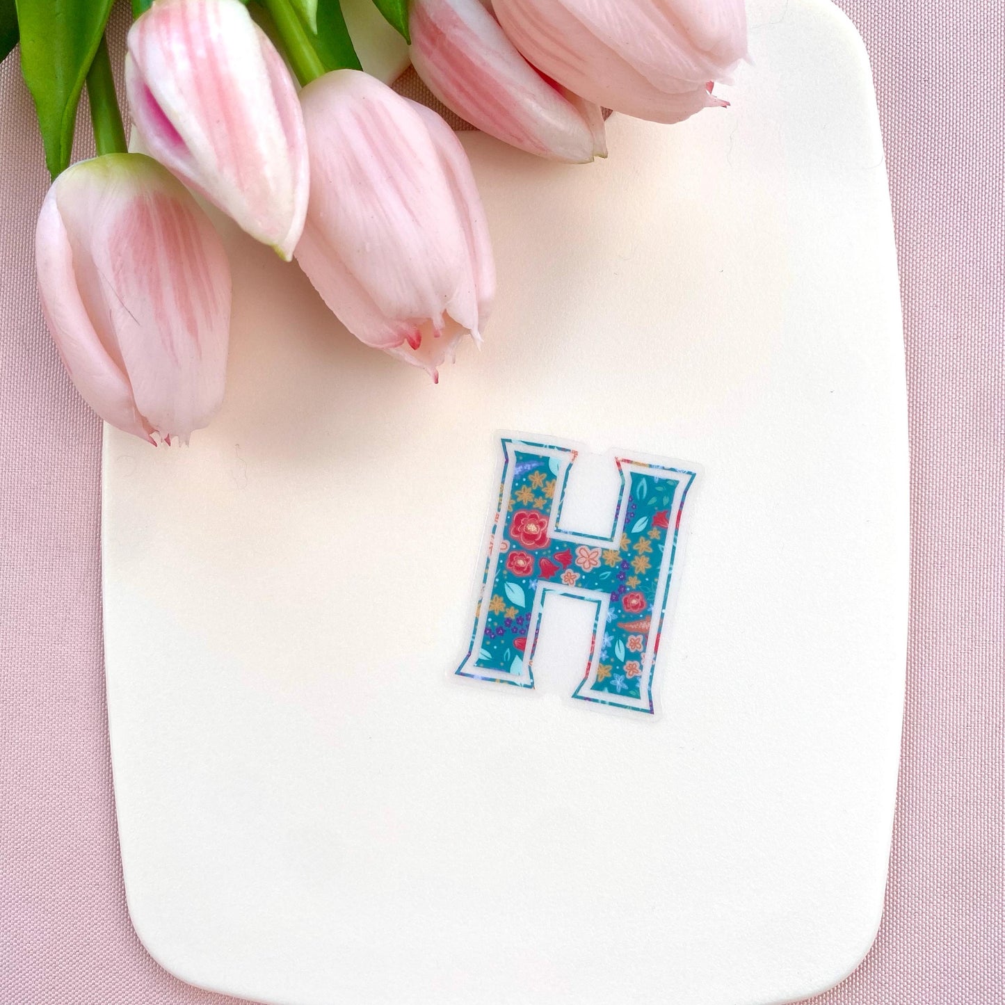 Letter 'H' sticker with a floral pattern on a pink background with pink tulips.