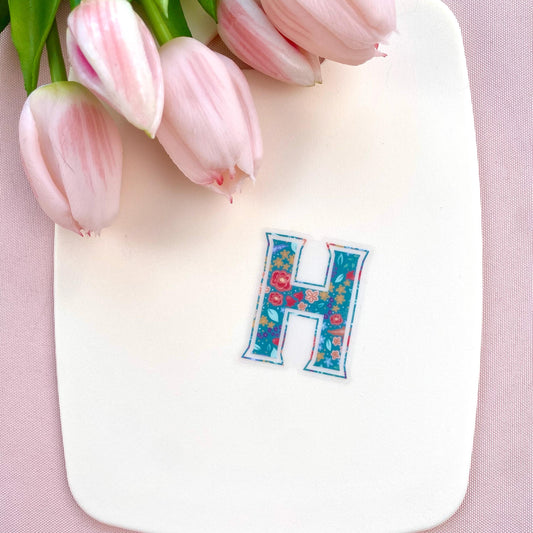 Letter 'H' sticker with a floral pattern on a pink background with pink tulips.