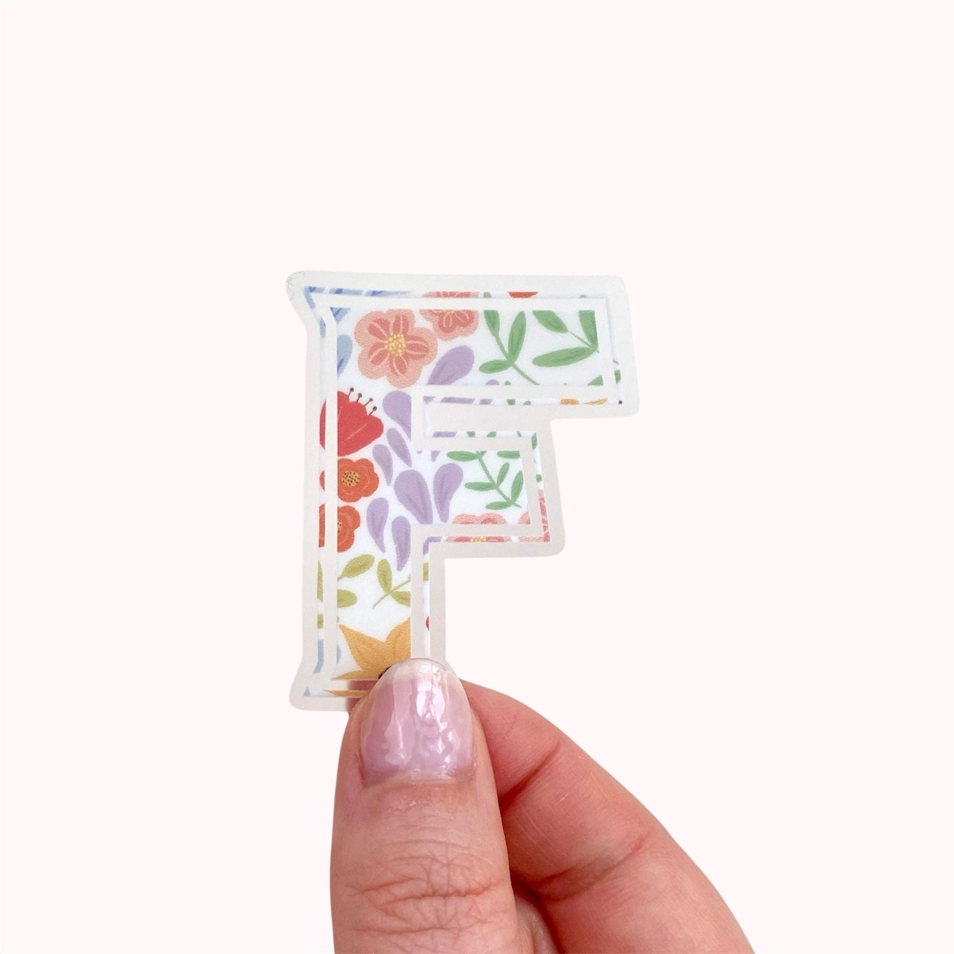 Floral letter 'F' clear sticker held by a hand against a white background