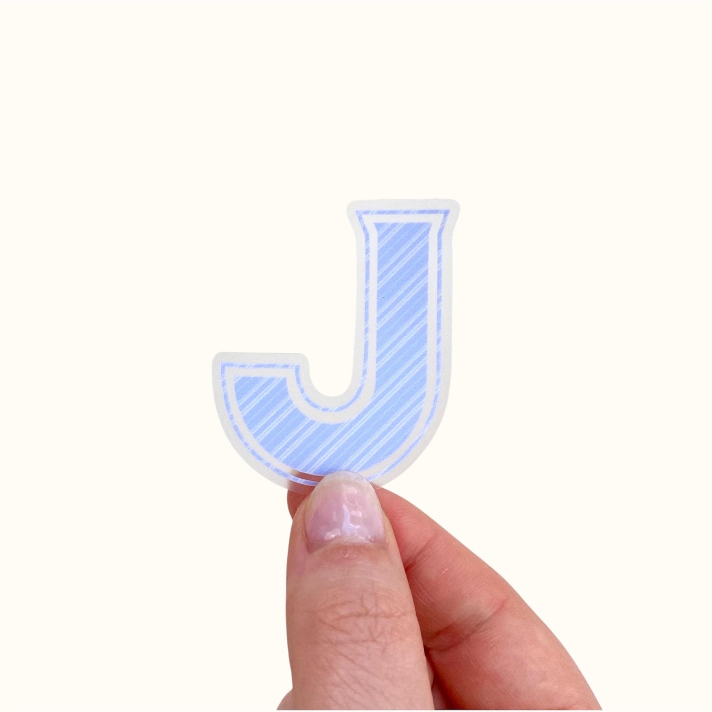 Hand holding a blue striped letter 'J' sticker on a white background