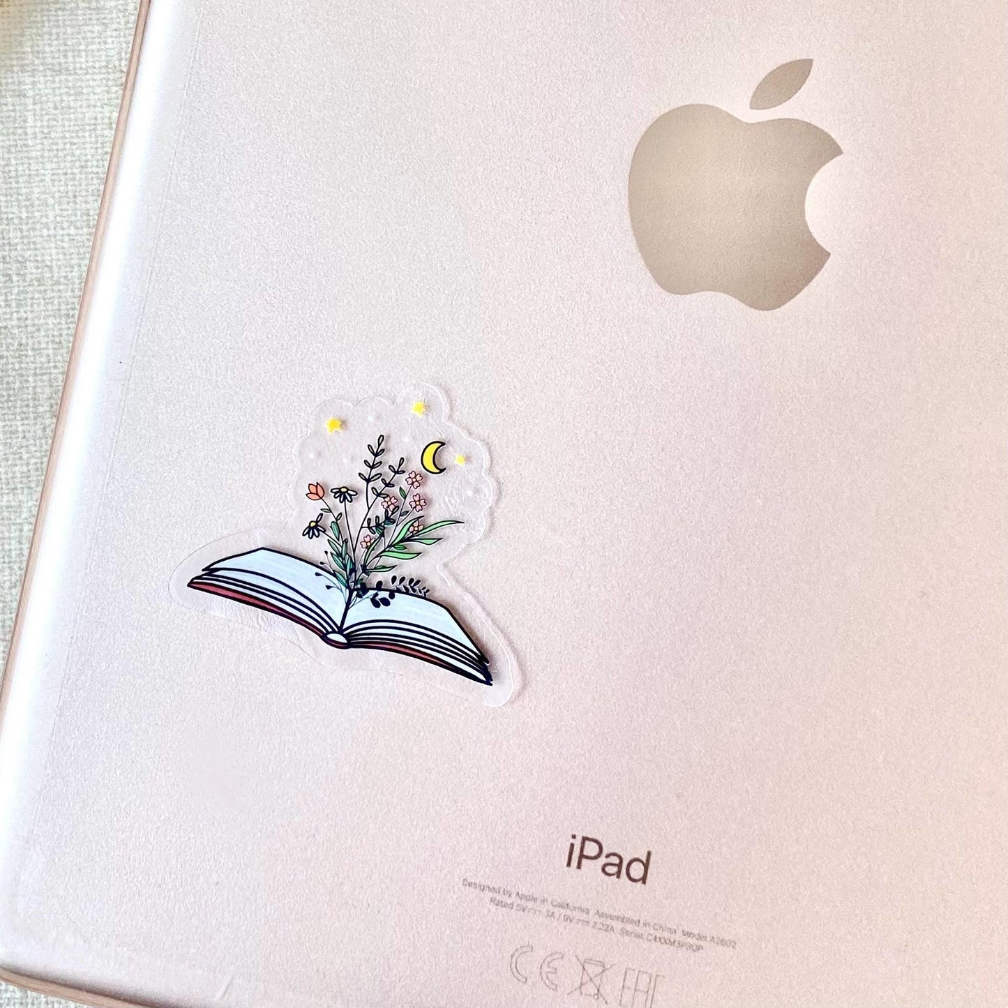 Decorative sticker of an open book with floral designs on the back of a rose gold ipad