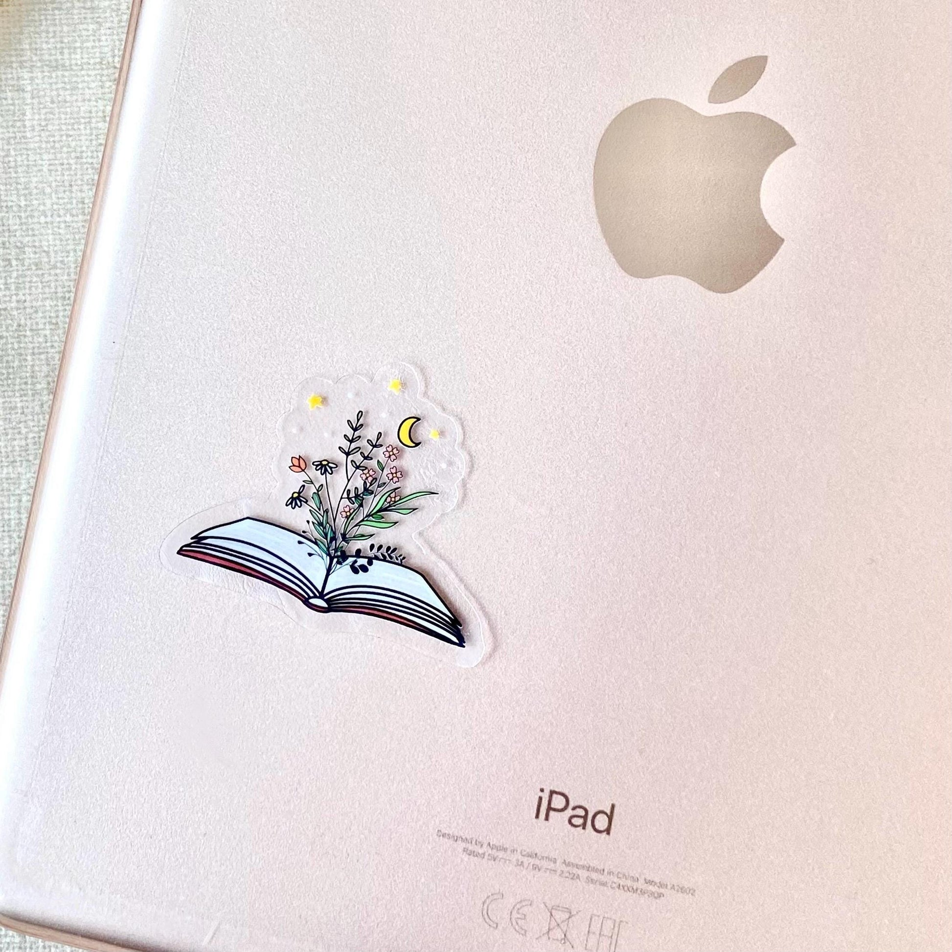 Decorative sticker of an open book with floral designs on the back of a rose gold ipad