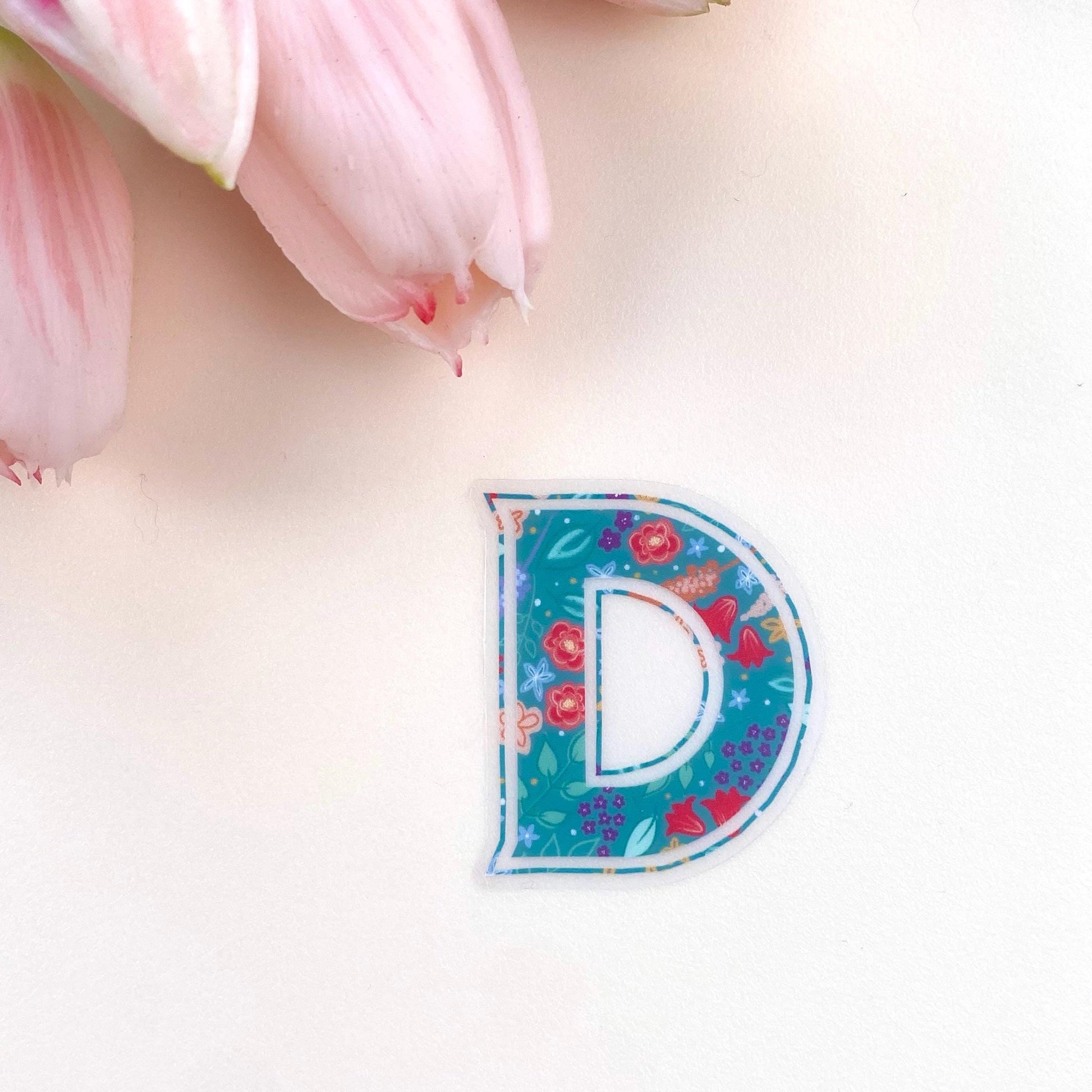Colourful letter 'D' sticker on a light pink background with tulips