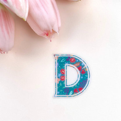 Colourful letter 'D' sticker on a light pink background with tulips