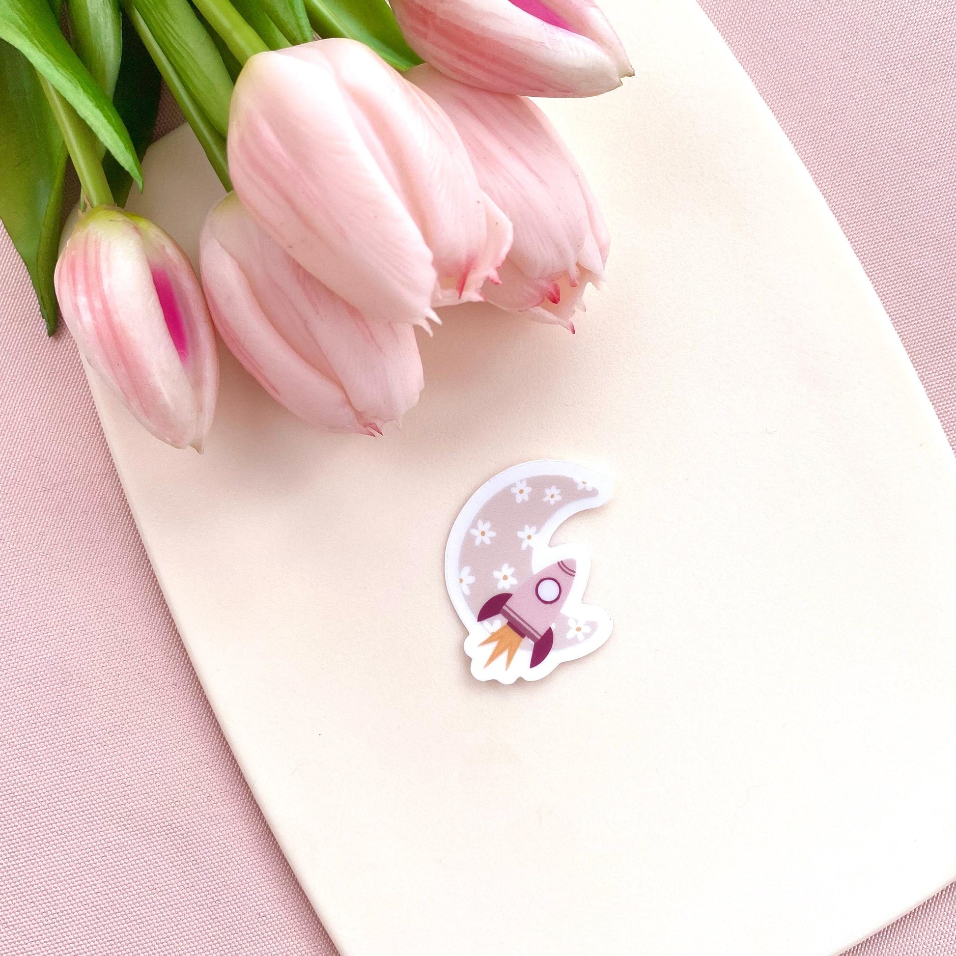 Decorative sticker with pink rocket and floral moon design on a white background with pink tulips