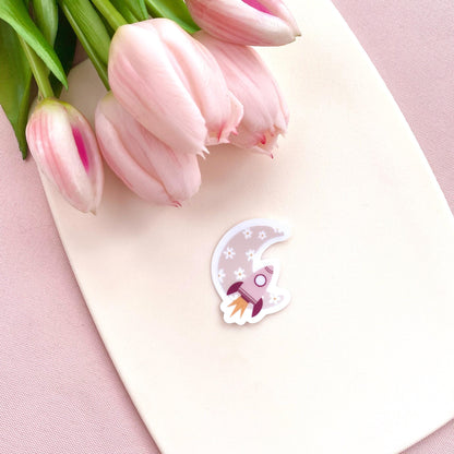 Decorative sticker with pink rocket and floral moon design on a white background with pink tulips