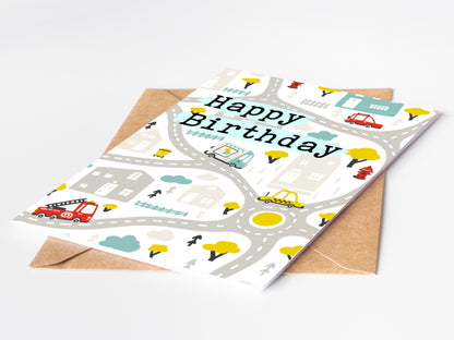 Birthday card with road map design and 'Happy Birthday' text, featuring vehicles, houses, trees and roads on a white background.