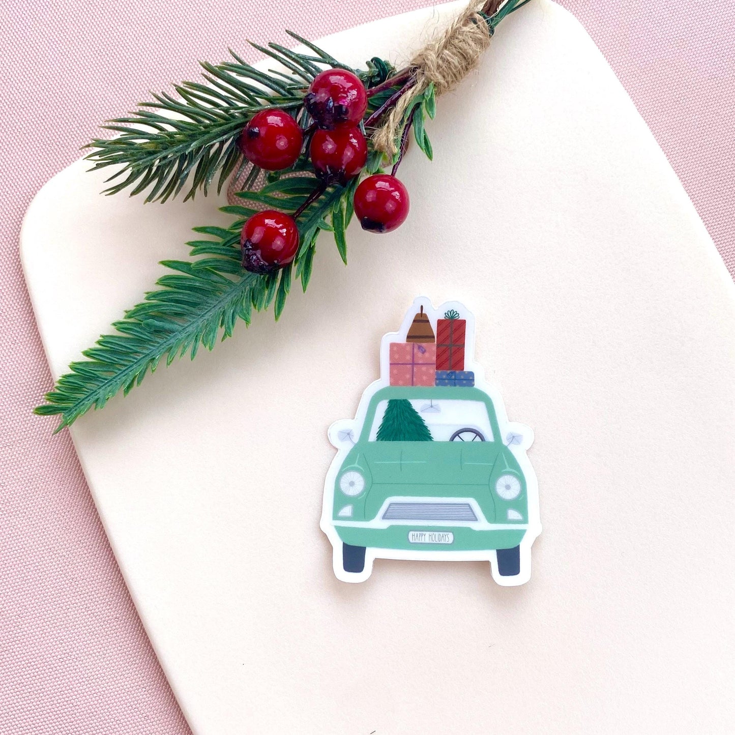 Sticker of a green car with Christmas decorations on a white surface with a pink background