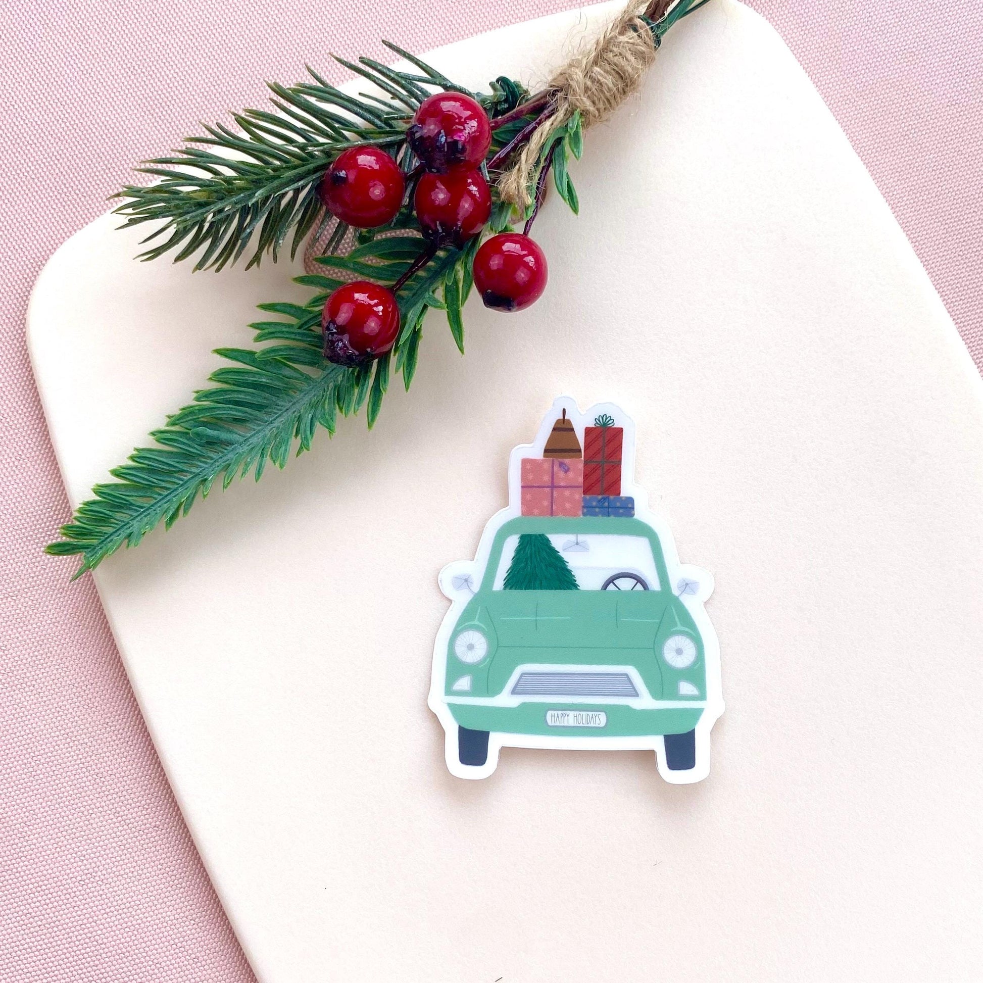 Sticker of a green car with Christmas decorations on a white surface with a pink background