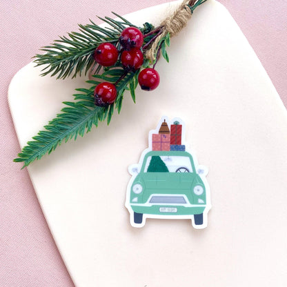 Sticker of a green car with Christmas decorations on a white surface with a pink background