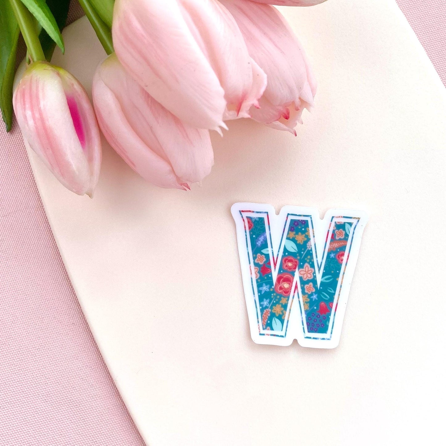Floral letter 'W' sticker on a pink surface with tulips