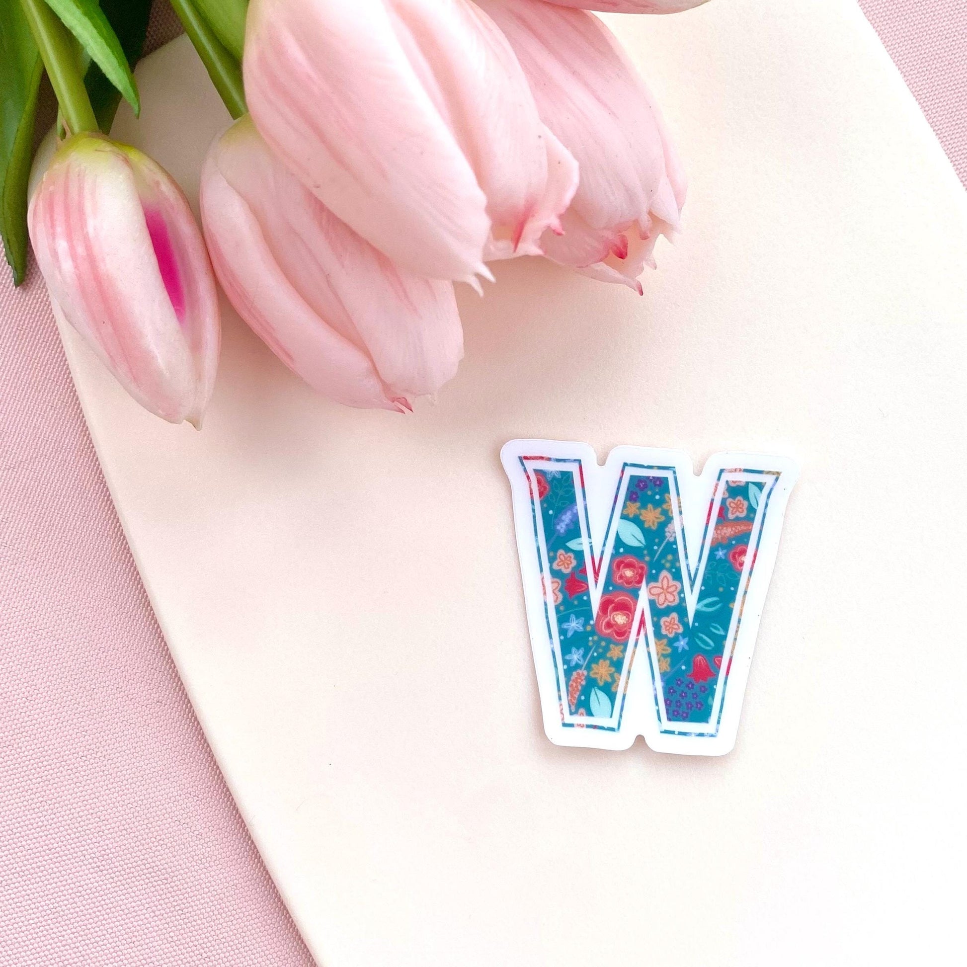 Floral letter 'W' sticker on a pink surface with tulips