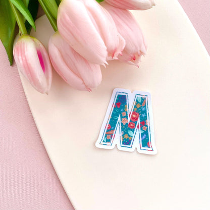 Floral letter 'M' sticker on a pink surface with pink tulips