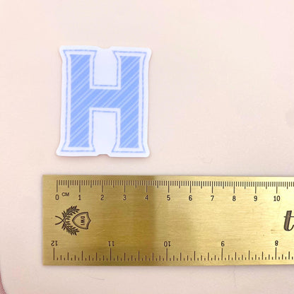 Letter 'H' sticker with a ruler for scale on a beige background