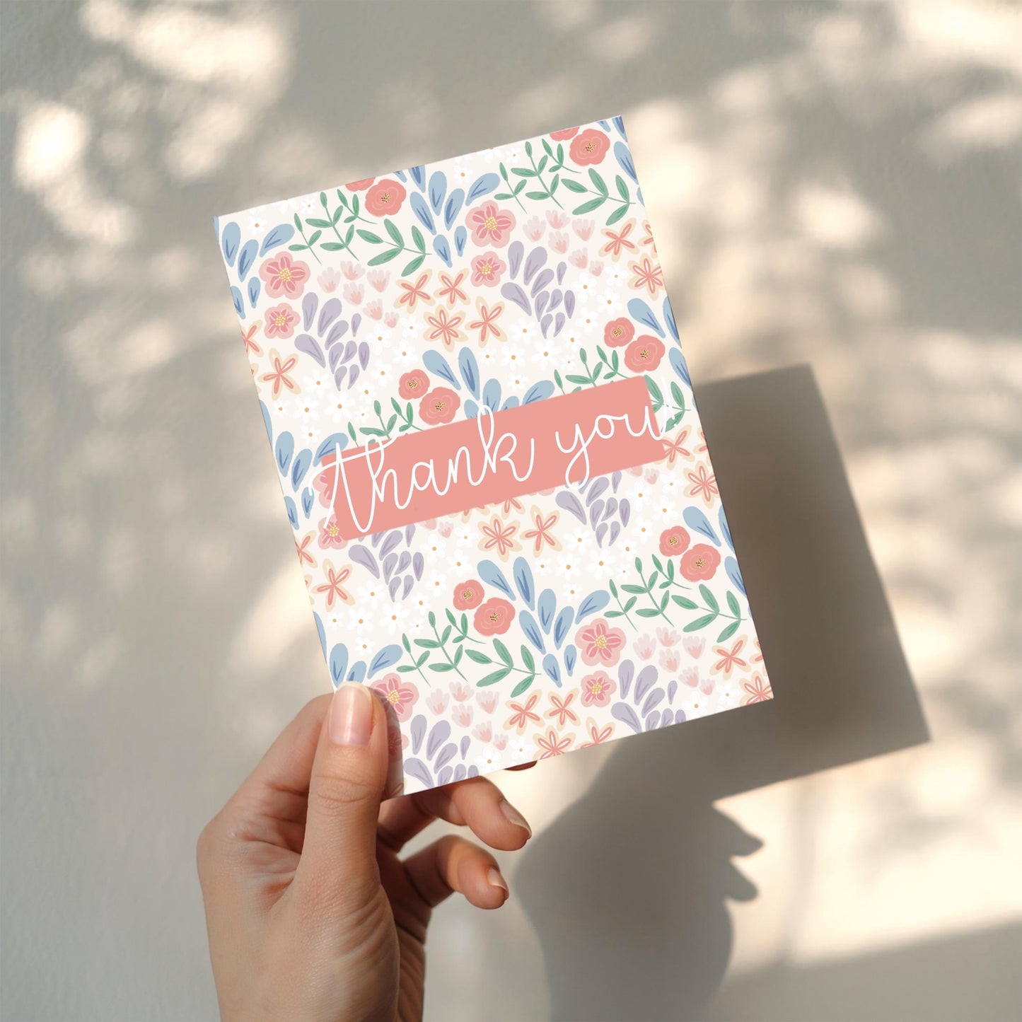 Hand holding a floral card with 'thank you' text against a neutral background