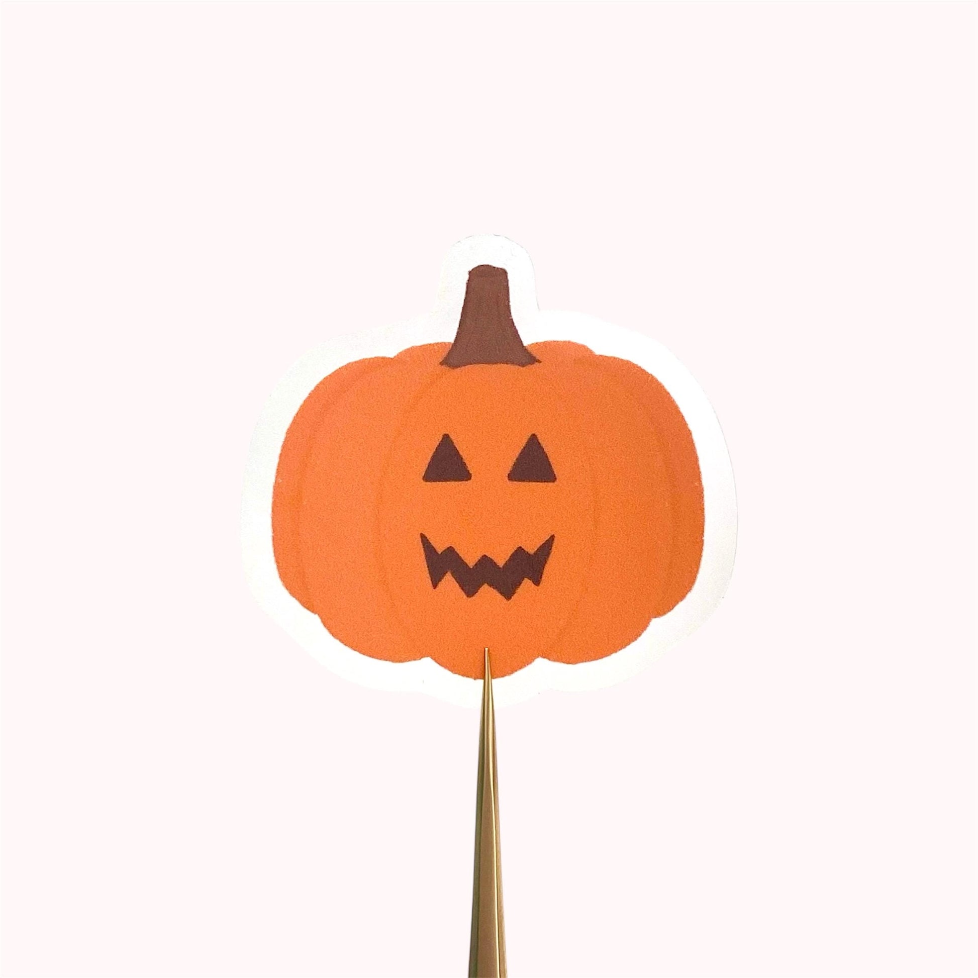 Orange jack-o-lantern pumpkin sticker held against a pink background.