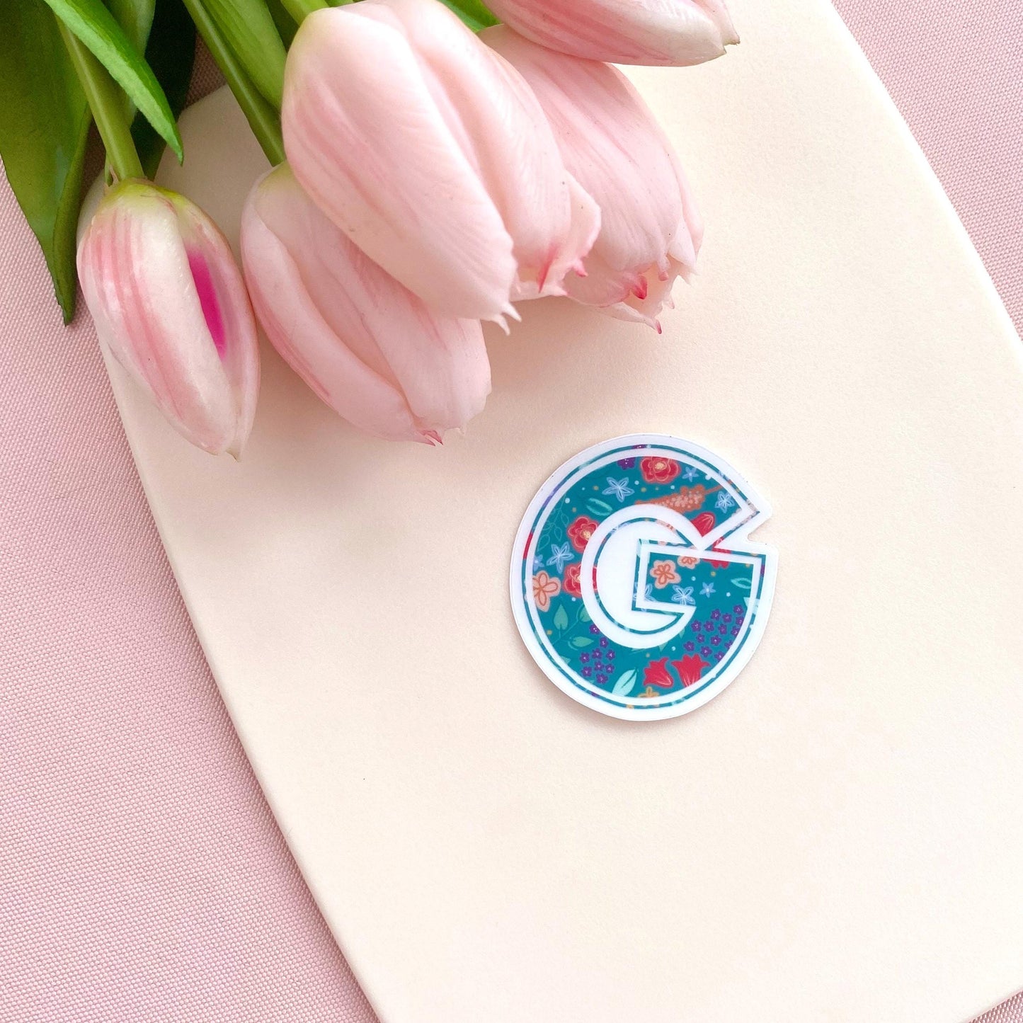 Decorative letter 'G' sticker with floral design on a light background with pink tulips