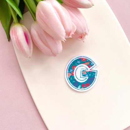Decorative letter 'G' sticker with floral design on a light background with pink tulips