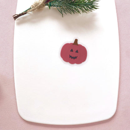Pink pumpkin-shaped sticker on a white plate with a pink background