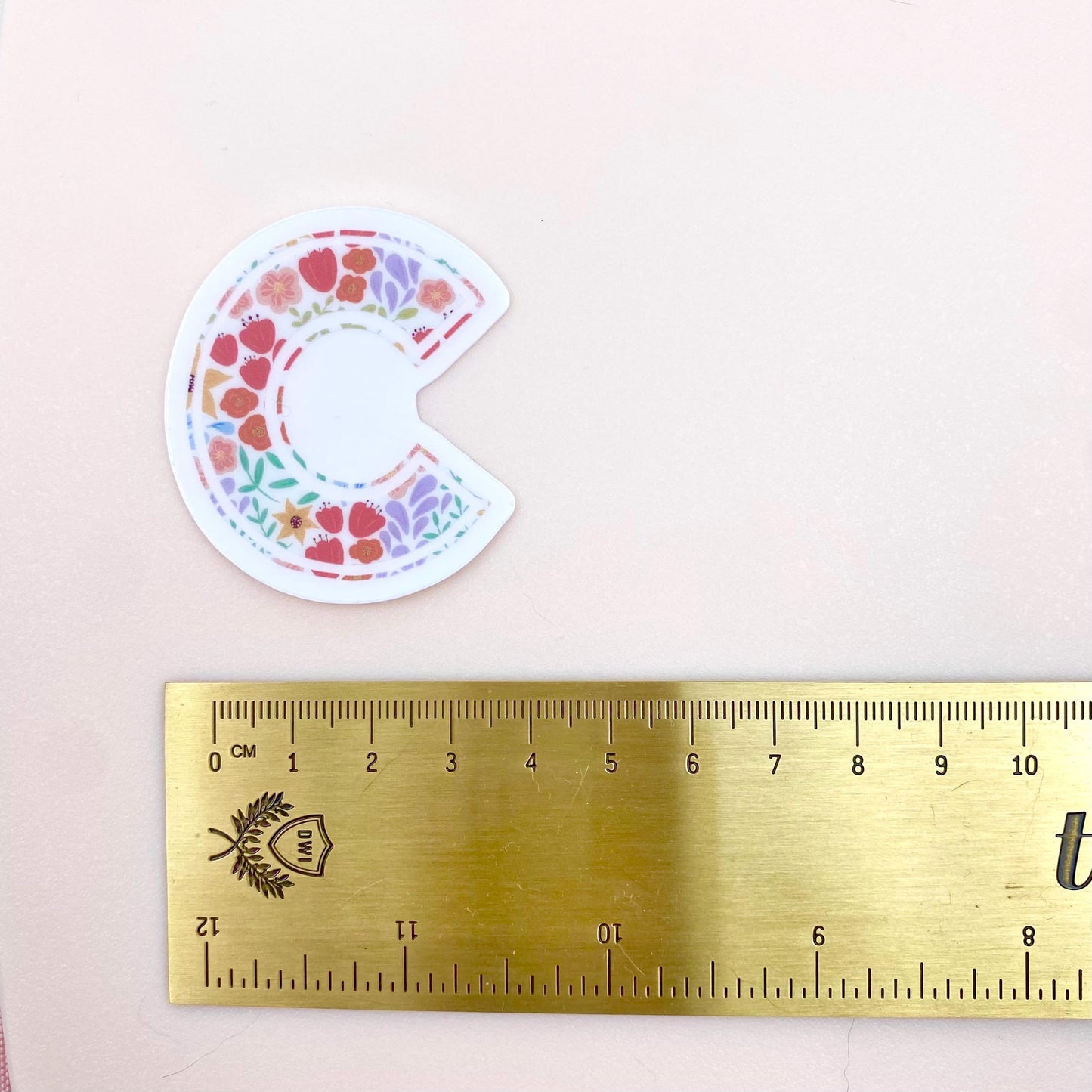 Floral-patterned letter 'C' sticker on a pink background with a gold ruler for scale.