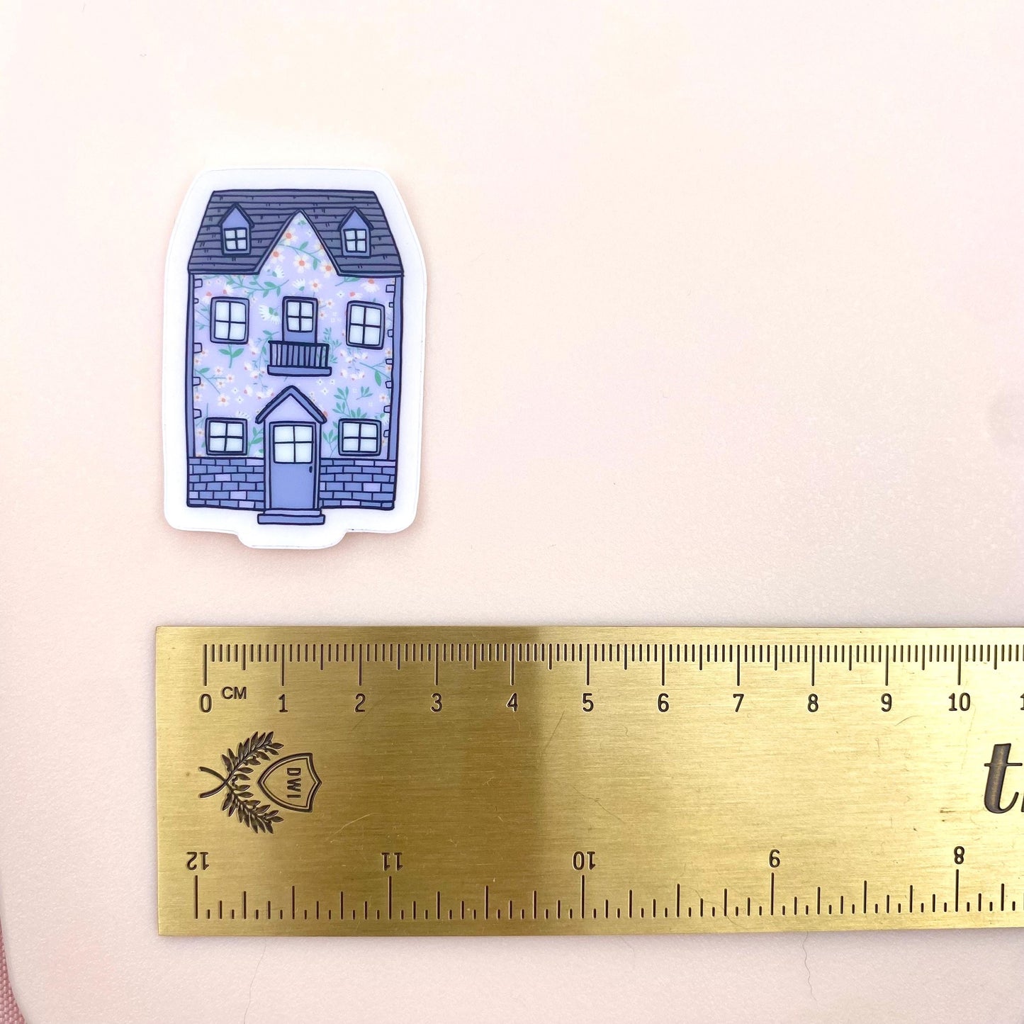 Sticker of a blue house with floral details next to a ruler on a beige background