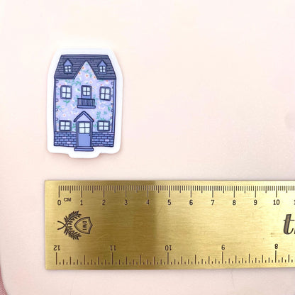 Sticker of a blue house with floral details next to a ruler on a beige background