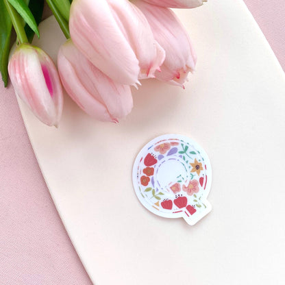Decorative letter 'Q' sticker with floral patterns on a light background with pink tulips.