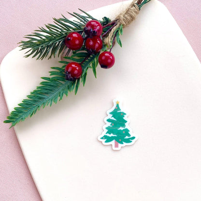 Decorative Christmas tree sticker with holly leaves and berries on a white surface.