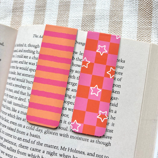 Two colourful striped and checkerboard bookmarks on an open book with a striped fabric background.