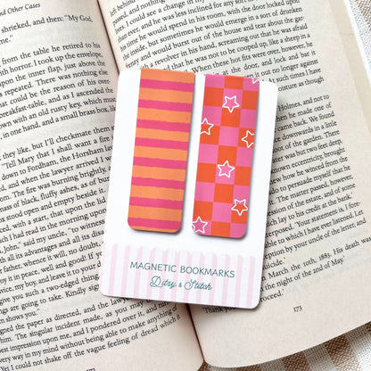 Magnetic bookmarks with pink and orange checkerboard and striped patterns on an open book with a striped background