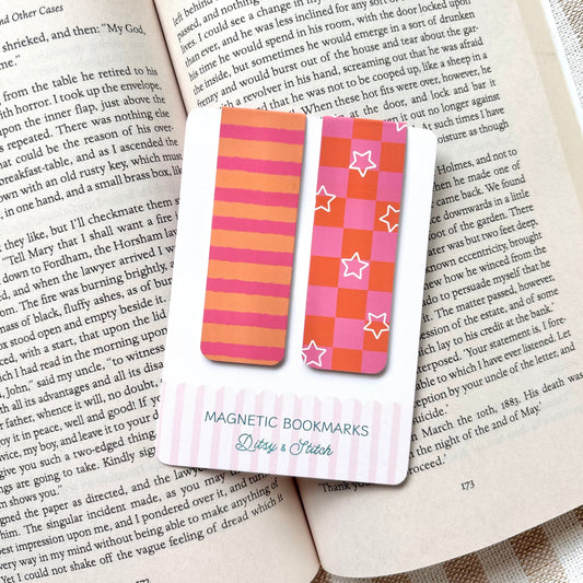 Magnetic bookmarks with pink and orange checkerboard and striped patterns on an open book with a striped background